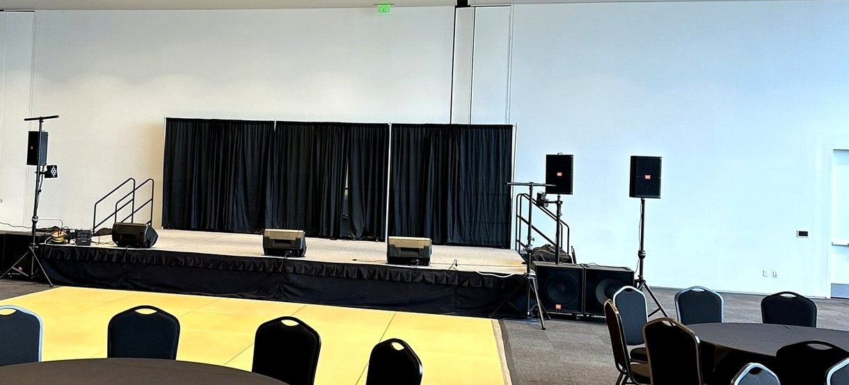 Corporate event room set before guests arrive with stage, stage monitors, speakers on stands, and subwoofers